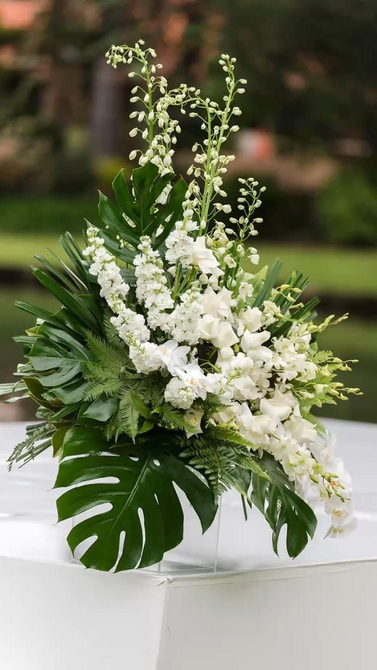 a vase filled with white flowers and greenery