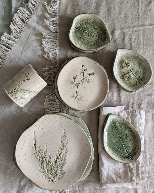 four plates and two bowls with plants on them sitting on a table cloth next to each other