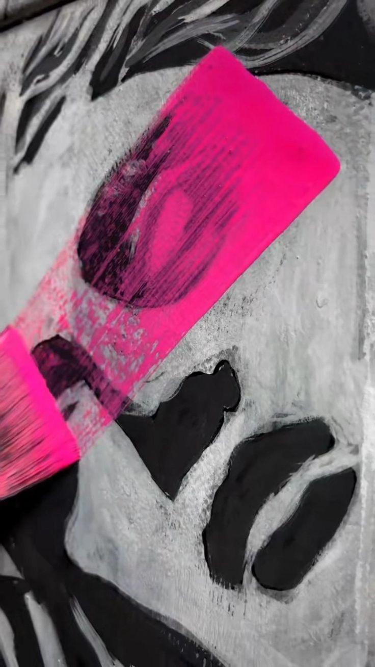 a close up of a pink and black painting on a wall with a brush in it's mouth