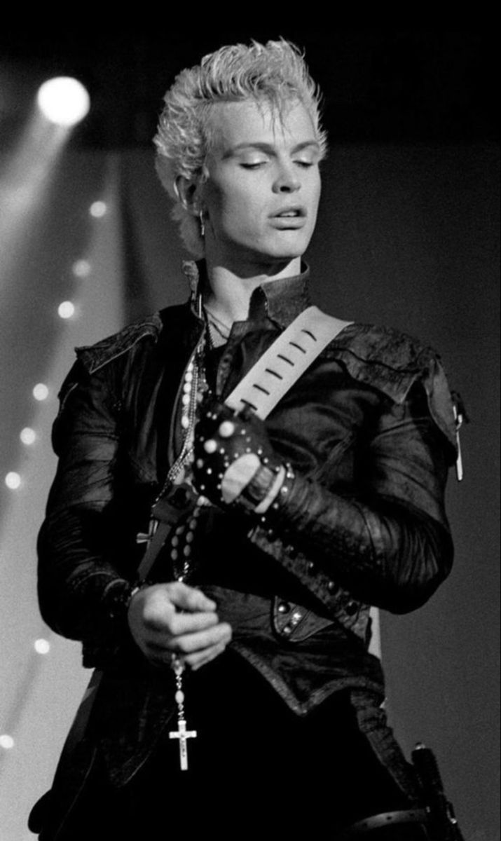 a woman standing in front of a microphone on stage with her arms crossed and wearing a cross around her neck