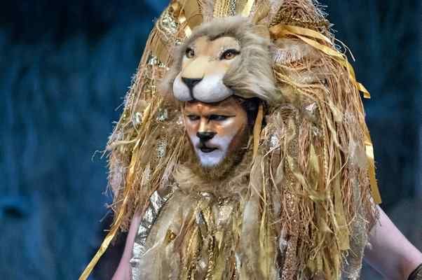 a man in a lion costume with his face painted gold and silver, walking down the runway