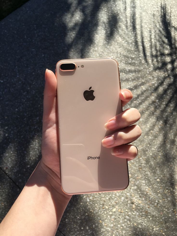 a person holding an iphone in their left hand and palm tree shadow on the ground