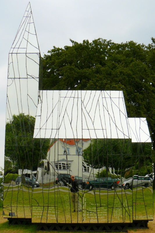 the reflection of a building in a mirror on a grass field with trees behind it