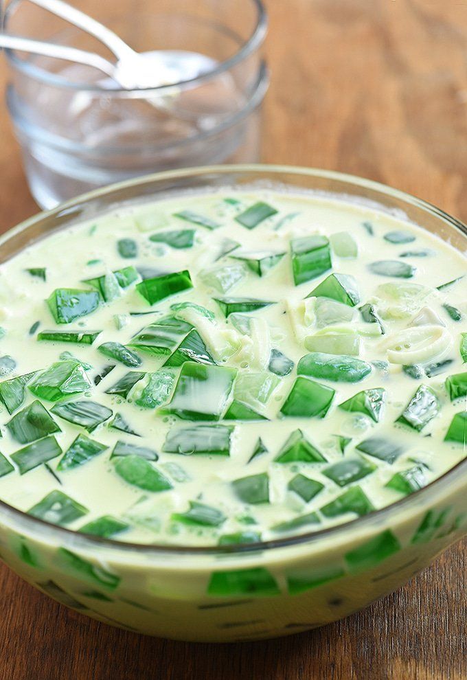 a glass bowl filled with green vegetables on top of a wooden table next to a spoon