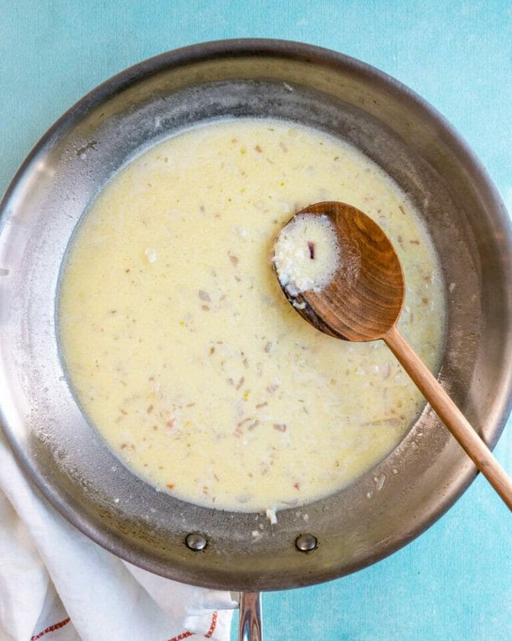 a wooden spoon is in a pan filled with cheese and sauces on a blue tablecloth