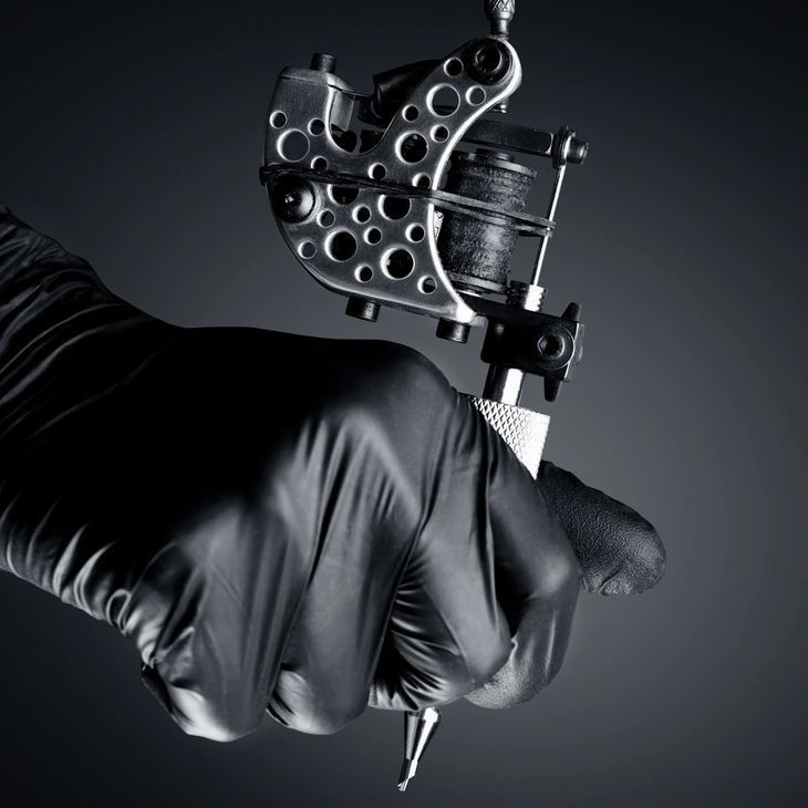 a person in black gloves is holding a tattoo machine with one arm and the other hand