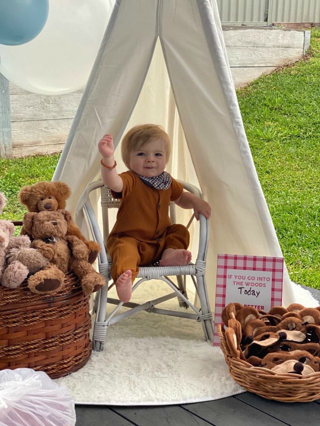 a little boy sitting in a chair next to some teddy bears and a teepee