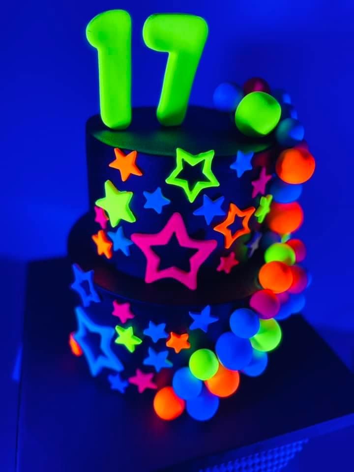 a birthday cake decorated with neon stars and numbers on it's side is lit up in the dark