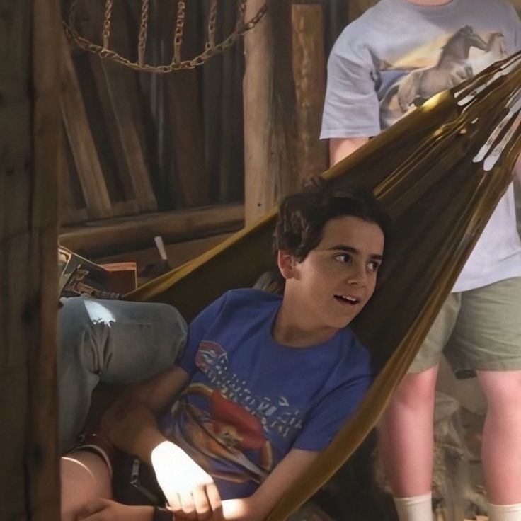 a young boy sitting in a hammock with his feet up on the ground