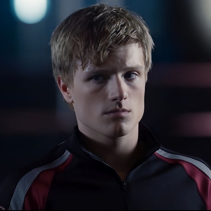 a young man with blonde hair wearing a black and red jacket in a dark room