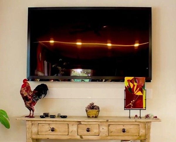 a tv mounted on the wall above a wooden table with two rooster figurines