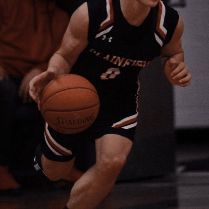 a young man dribbling a basketball on top of a wooden floor in a gym