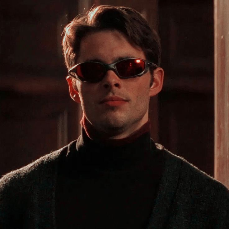 a man wearing sunglasses and a black turtle neck sweater in a dark room with wooden doors