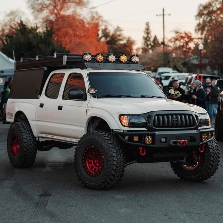 a white pick up truck with red rims parked in a parking lot next to other cars