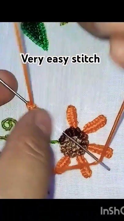 someone is stitching an orange flower on a white piece of fabric with knitting needles