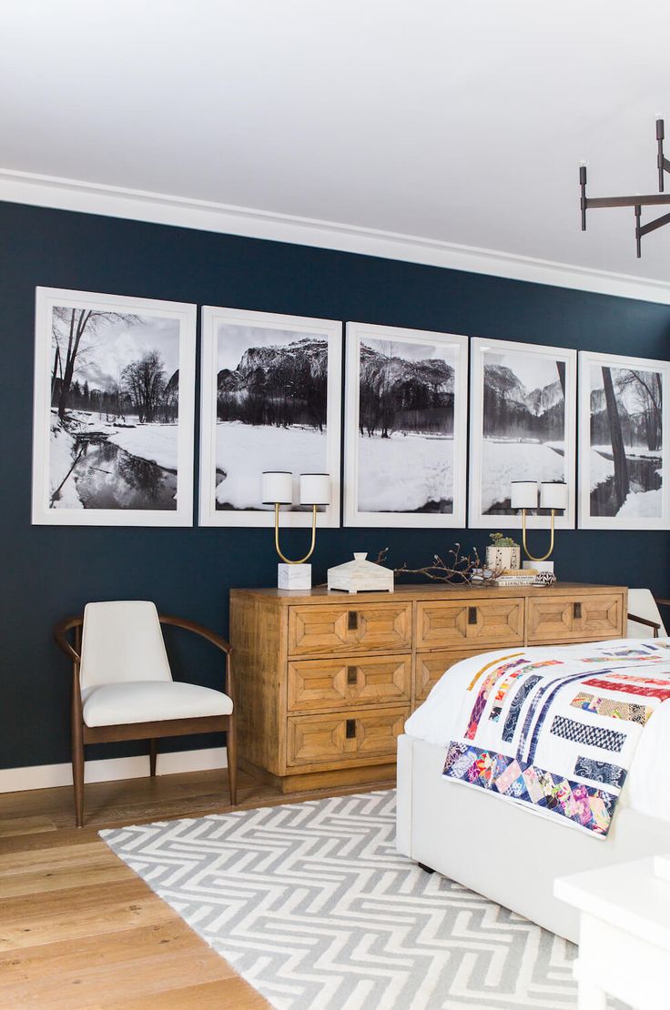 a bedroom with black walls and pictures on the wall above the bed, along with a white chair