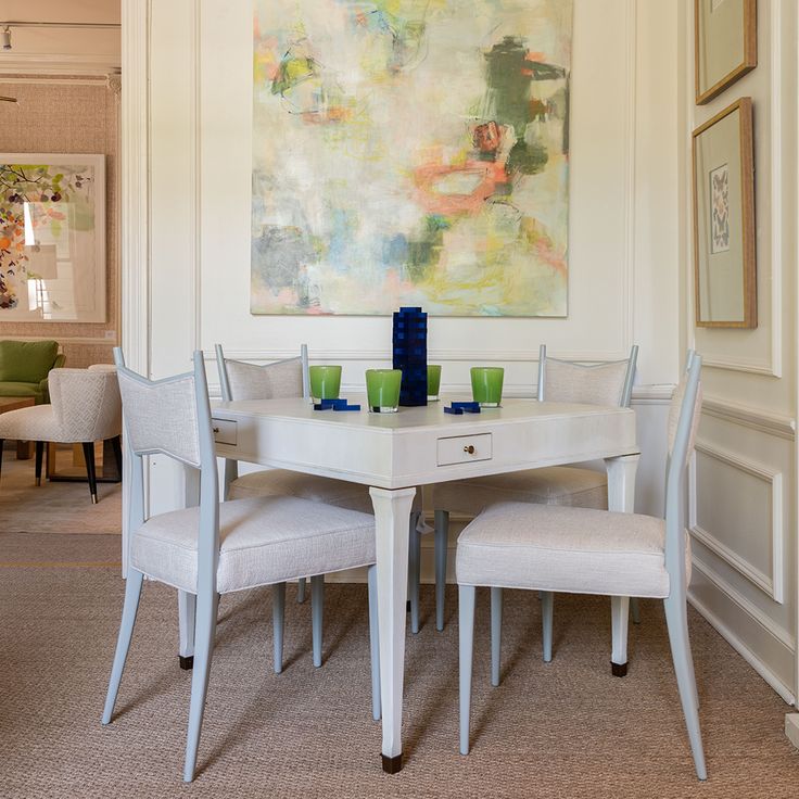 a white table with four chairs and a painting on the wall behind it in a dining room