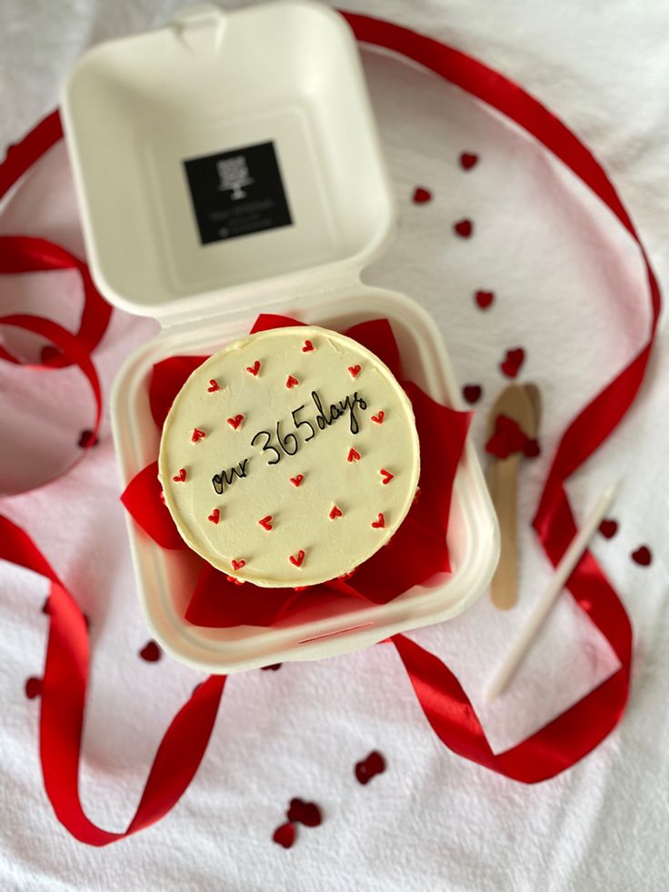 a birthday cake in a box with a red ribbon around it and an empty container on the table