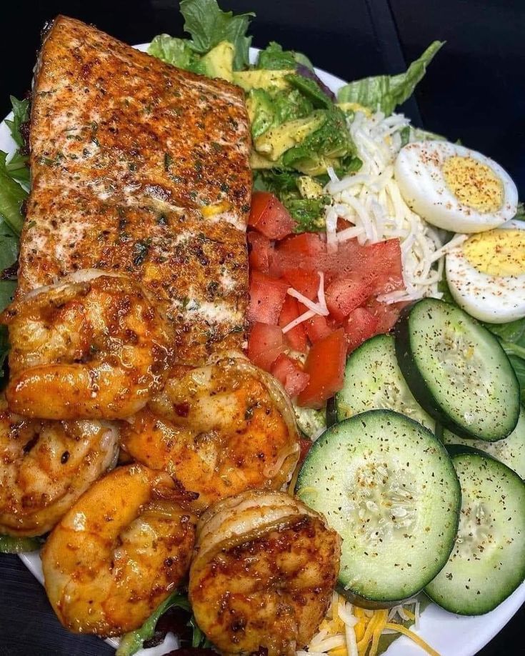 a white plate topped with lots of food next to cucumbers and tomatoes on top of a table