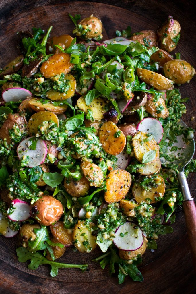 a wooden bowl filled with lots of veggies on top of a table next to a spoon