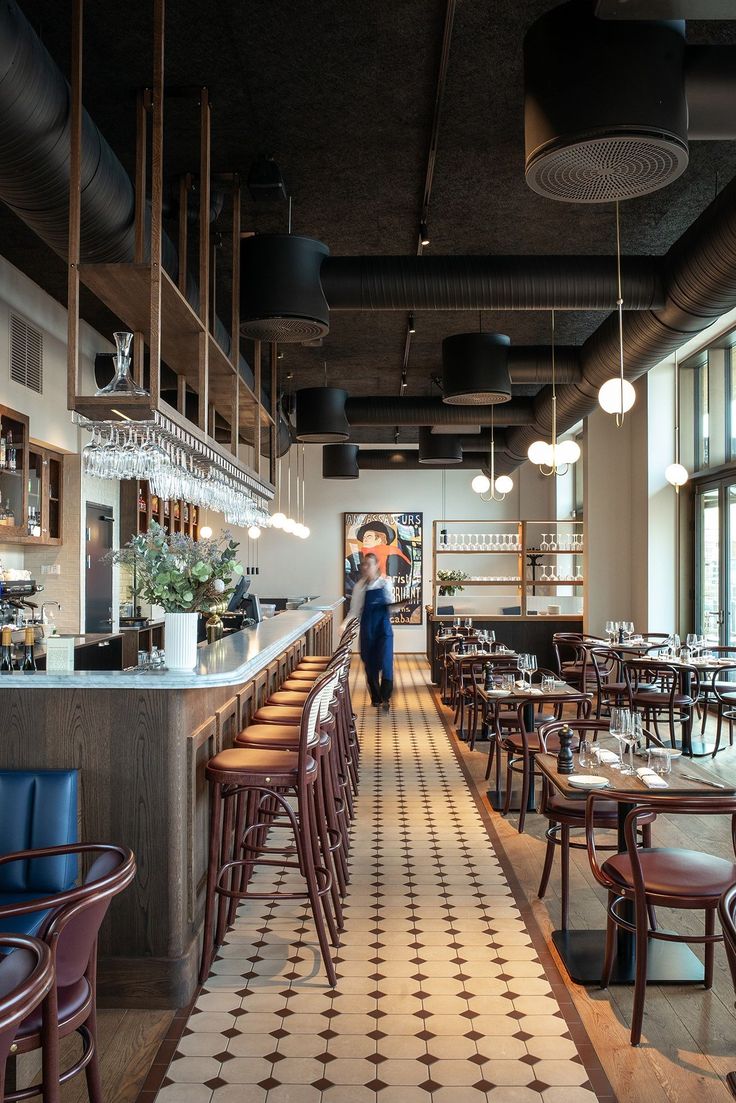 an empty restaurant with tables and chairs in front of the counter, people are standing at the bar