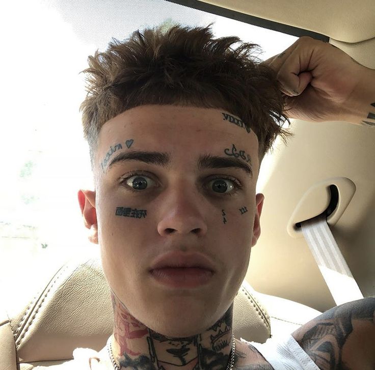 a man with tattoos on his face sitting in the back seat of a car looking at the camera