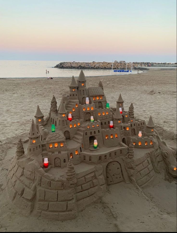 a sand castle on the beach with lights in it's windows and some water behind it