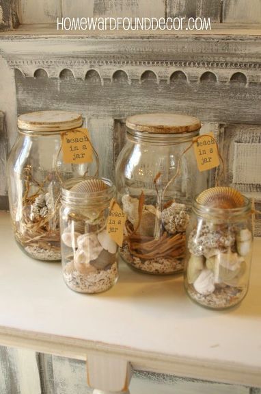 four jars filled with sand and shells on top of a table