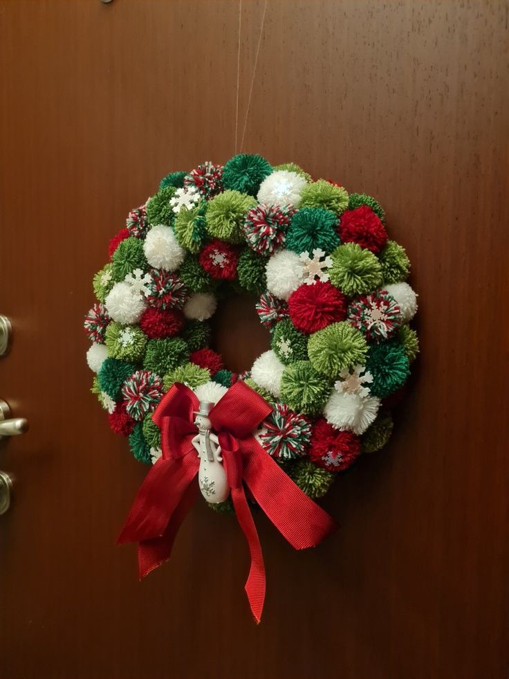 a christmas wreath hanging on a door with red ribbon and pom - poms