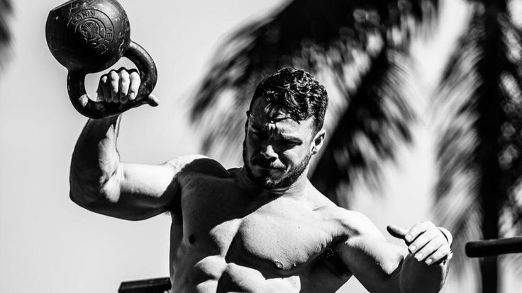 a shirtless man holding a kettle while standing in front of palm trees