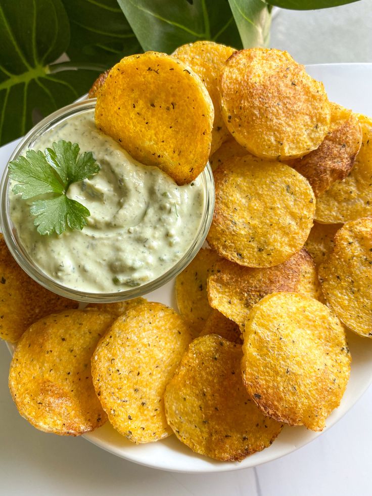 a white plate topped with potato chips and dipping sauce next to green leafy leaves