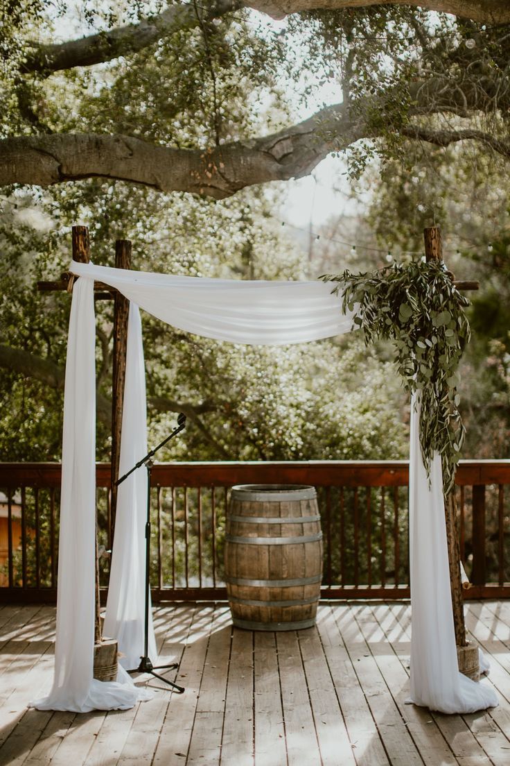 an outdoor ceremony setup with white draping and greenery on the top of a barrel