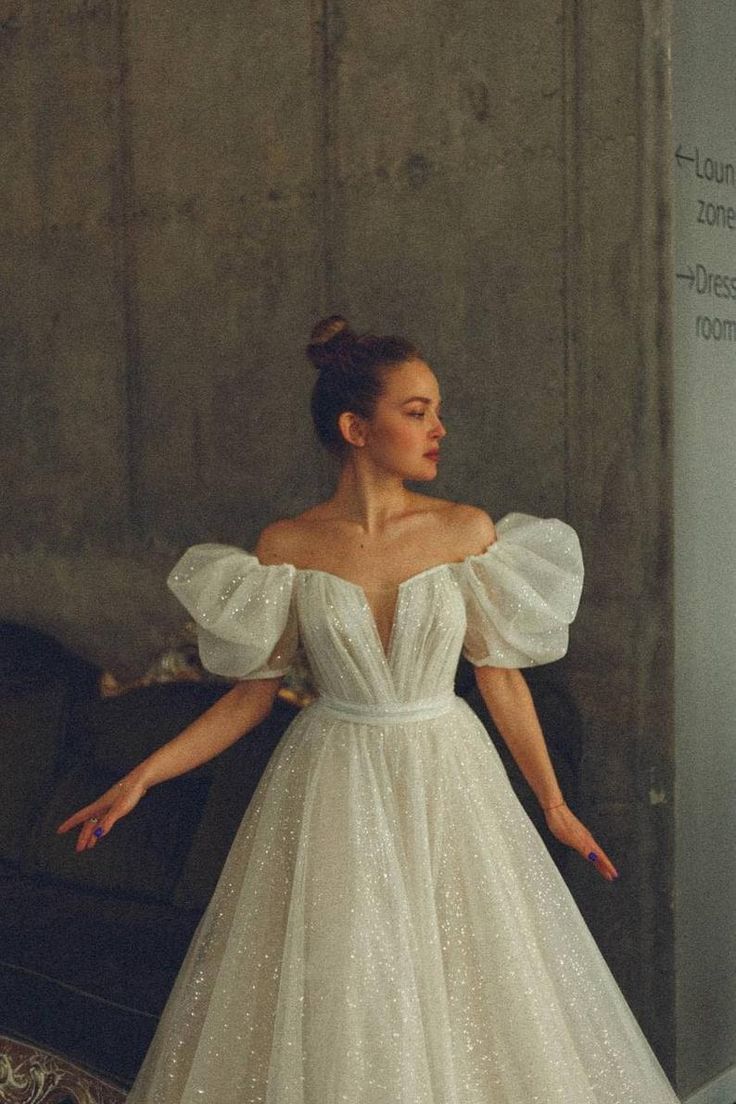 a woman in a white dress is standing near a wall