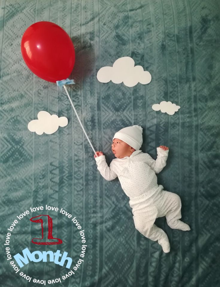 a baby laying on top of a bed holding a red balloon