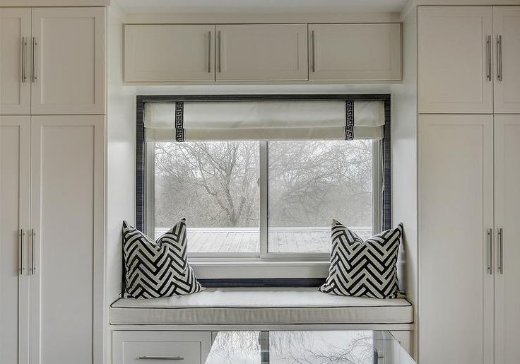 a window seat in the corner of a room with white cabinets and pillows on it