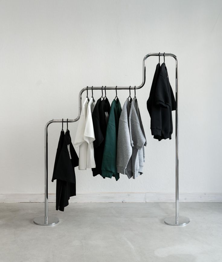 a rack with clothes hanging on it in front of a white wall next to a metal pole