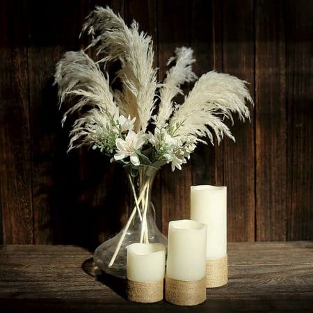 three white candles are sitting on a table with some flowers in the vase and feathers