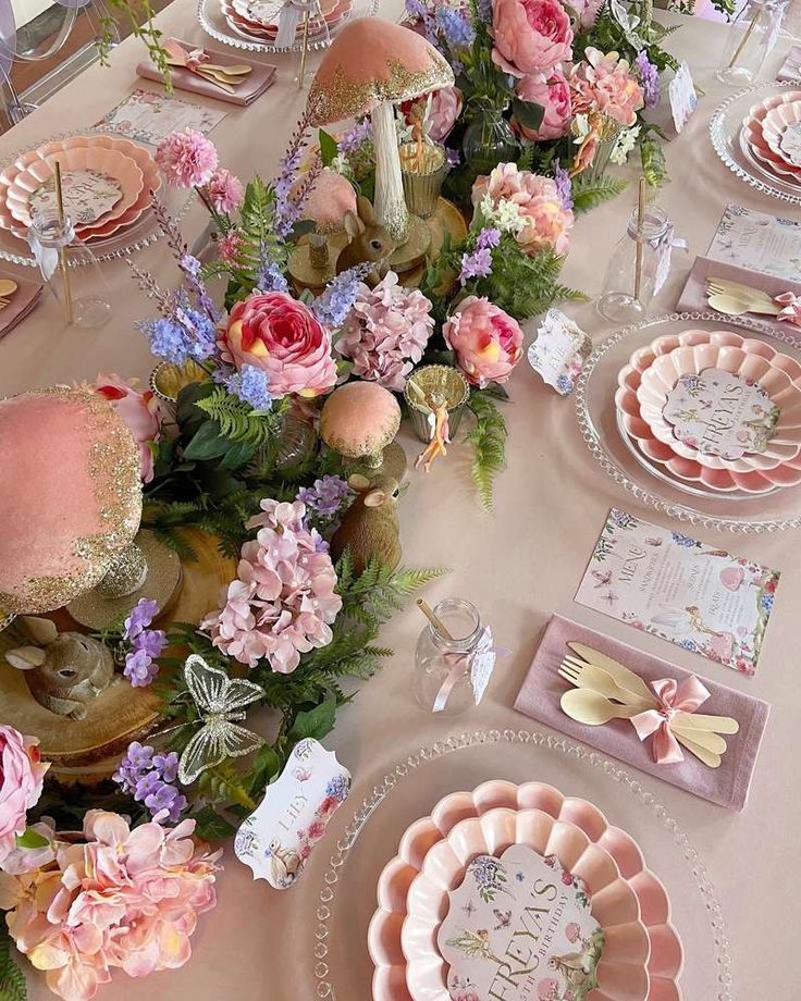 the table is set with pink flowers and plates