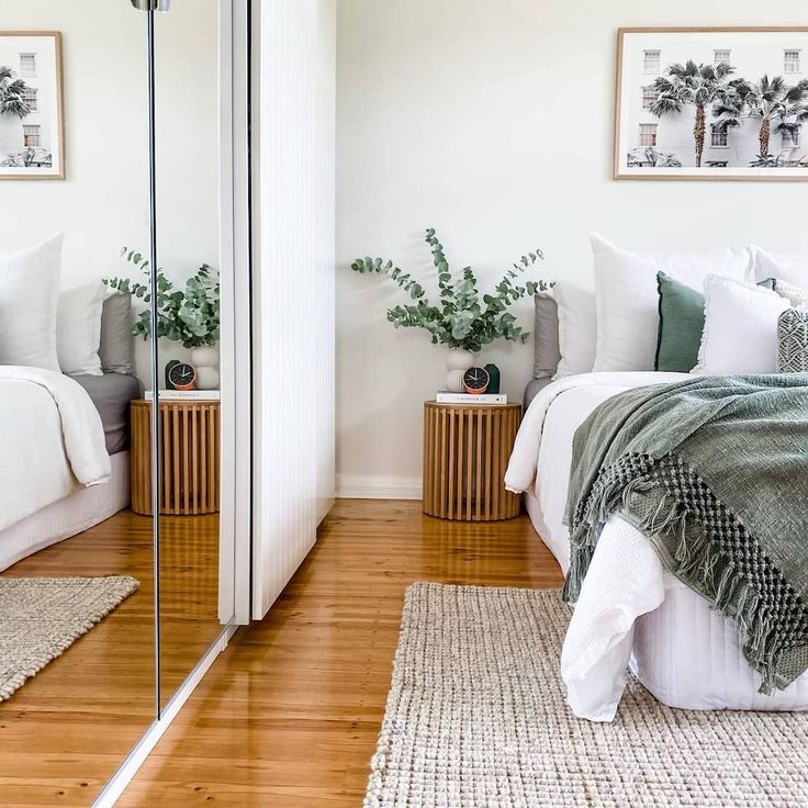 a bedroom with white walls and wood flooring is pictured in this image, there are plants on either side of the bed