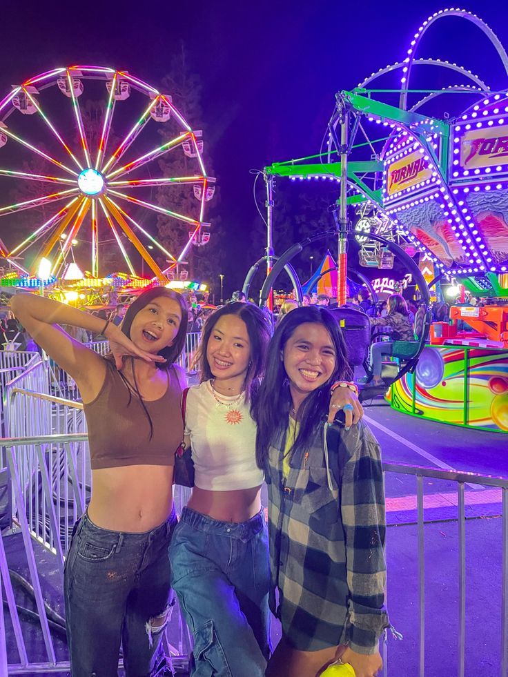 two women standing next to each other in front of a carnival ride and ferris wheel