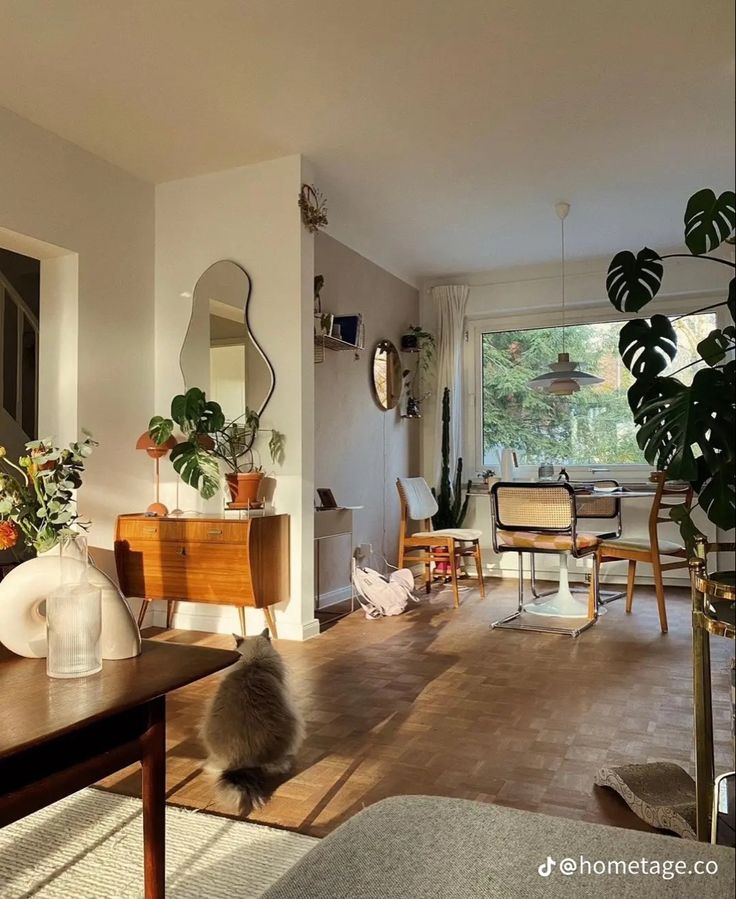 a living room filled with lots of furniture and plants on top of wooden flooring