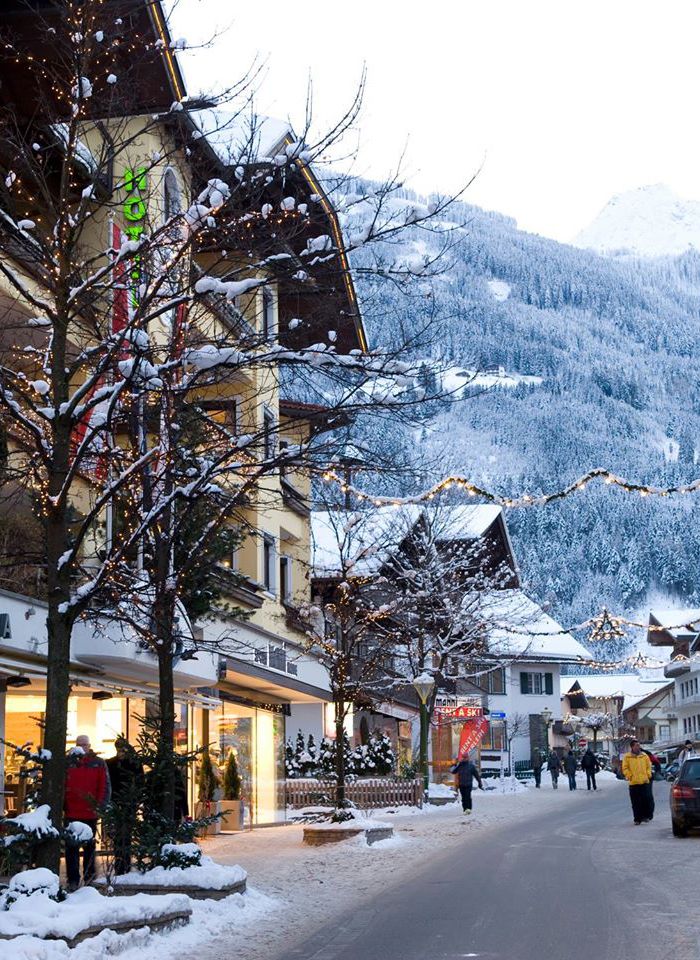 people are walking down the street in front of shops on a snowy day with mountains in the background