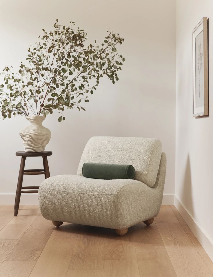 a white chair sitting in front of a vase on top of a hard wood floor