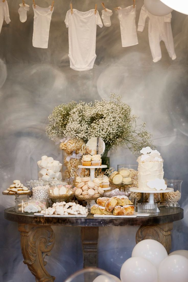 a table topped with lots of desserts next to white balloons and bundts