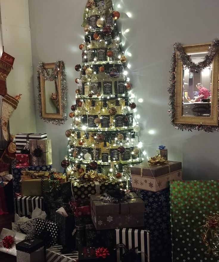 a christmas tree with presents under it in a living room next to a wall decorated with pictures and lights