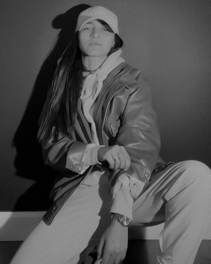 black and white photograph of a woman sitting on a stool with her eyes closed wearing a hat