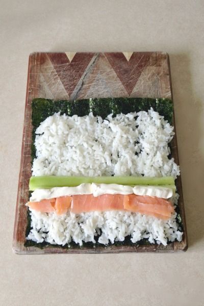 sushi with rice, cucumber and salmon on a wooden cutting board sitting on a table