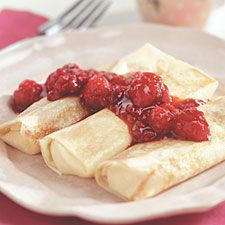 crepes with raspberries on top and sauce in the middle sitting on a plate