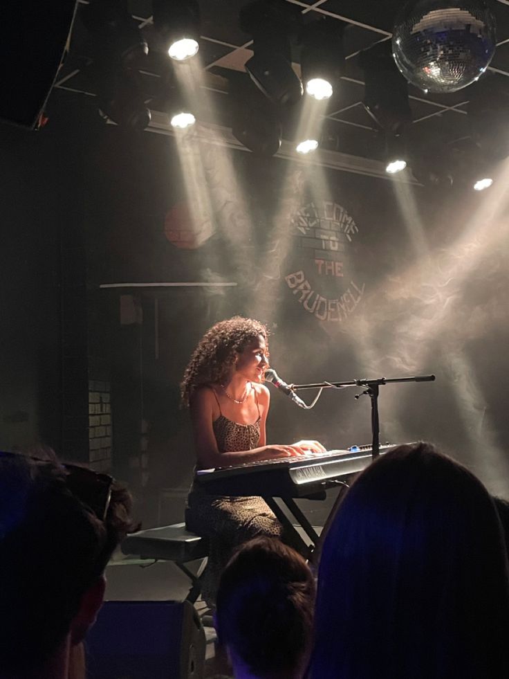 a woman sitting at a keyboard in front of a microphone on stage with lights behind her