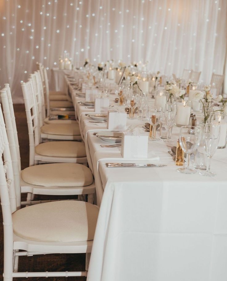 a long table with white chairs and candles